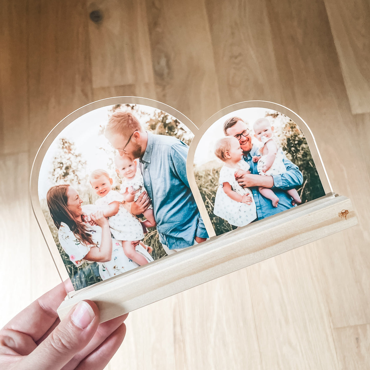 Beautiful Double Arch Plaque for Father's Day a heart-shaped custom acrylic photo plaque with two arches, each displaying a printed family photograph. The plaque has a light natural wood base and is photographed against a light wood floor background.