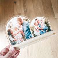Beautiful Double Arch Plaque for Father's Day a heart-shaped custom acrylic photo plaque with two arches, each displaying a printed family photograph. The plaque has a light natural wood base and is photographed against a light wood floor background.