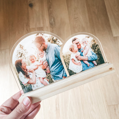 Beautiful Double Arch Plaque for Father's Day a heart-shaped custom acrylic photo plaque with two arches, each displaying a printed family photograph. The plaque has a light natural wood base and is photographed against a light wood floor background.