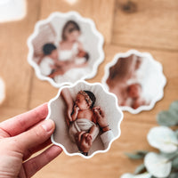 Hand holding a fridge magnet with a baby photo on a wooden surface with other similar magnets