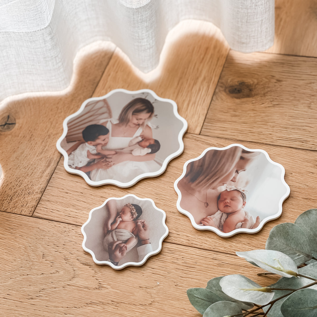 Three decorative fridge magnets with baby photos on a wooden surface with greenery.